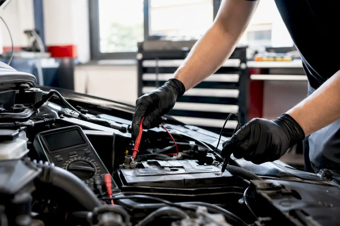 Hands testing car battery voltage with multimeter